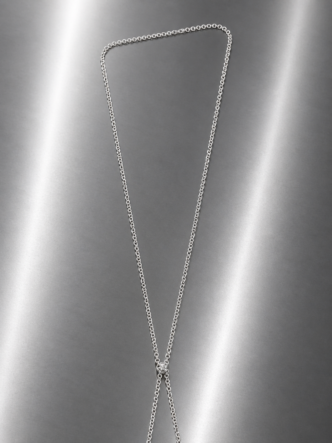 Near Earth Object | Silver chain necklace on a reflective gray surface