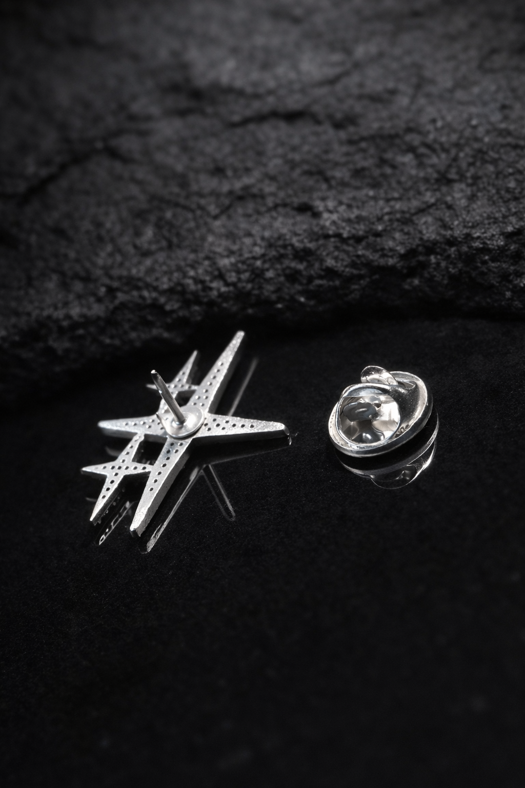 Near Earth Object | Star-shaped silver pin and round silver brooch on a dark textured surface