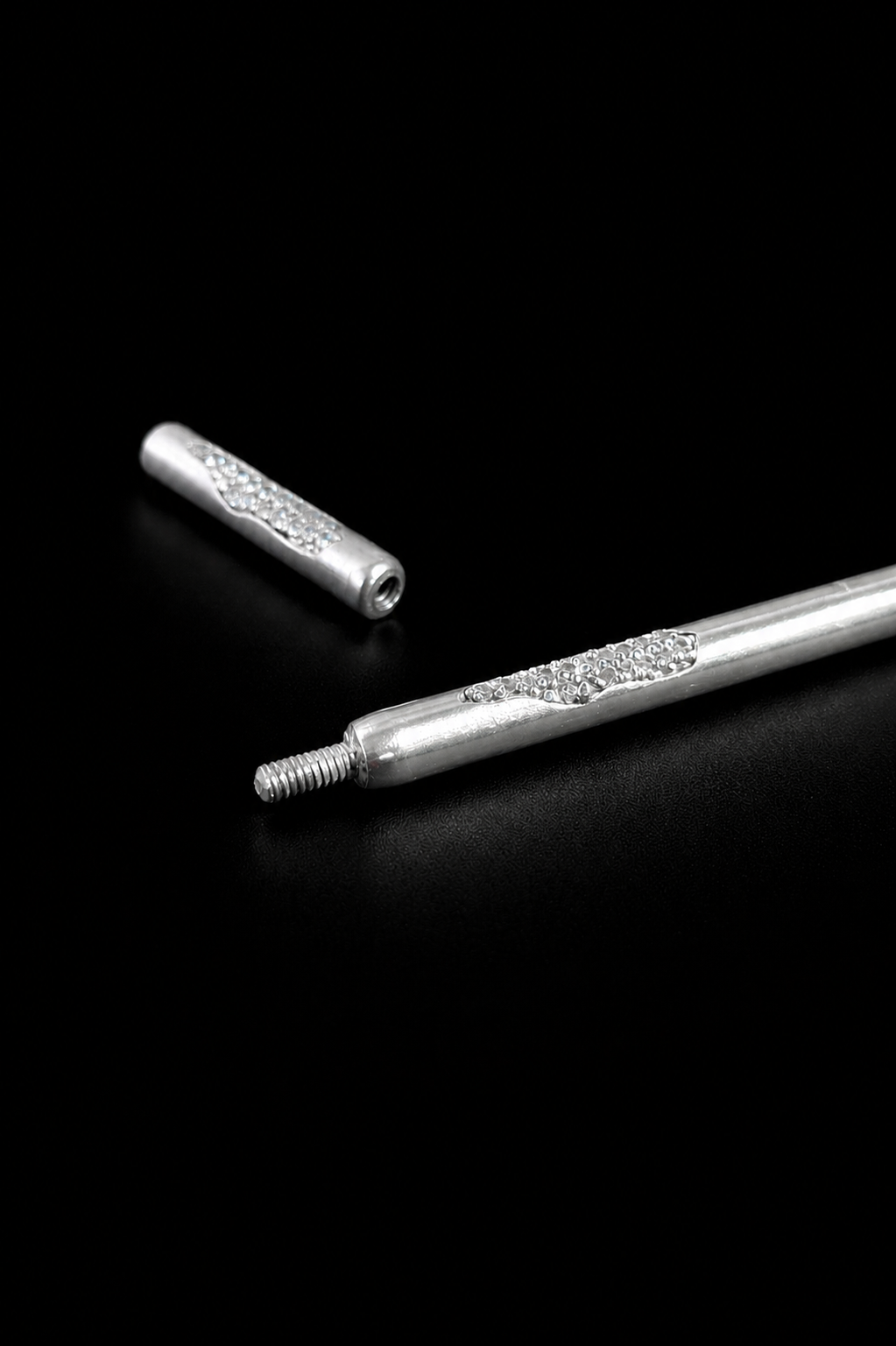 Near Earth Object | Two silver cylindrical objects with decorative elements on a black background