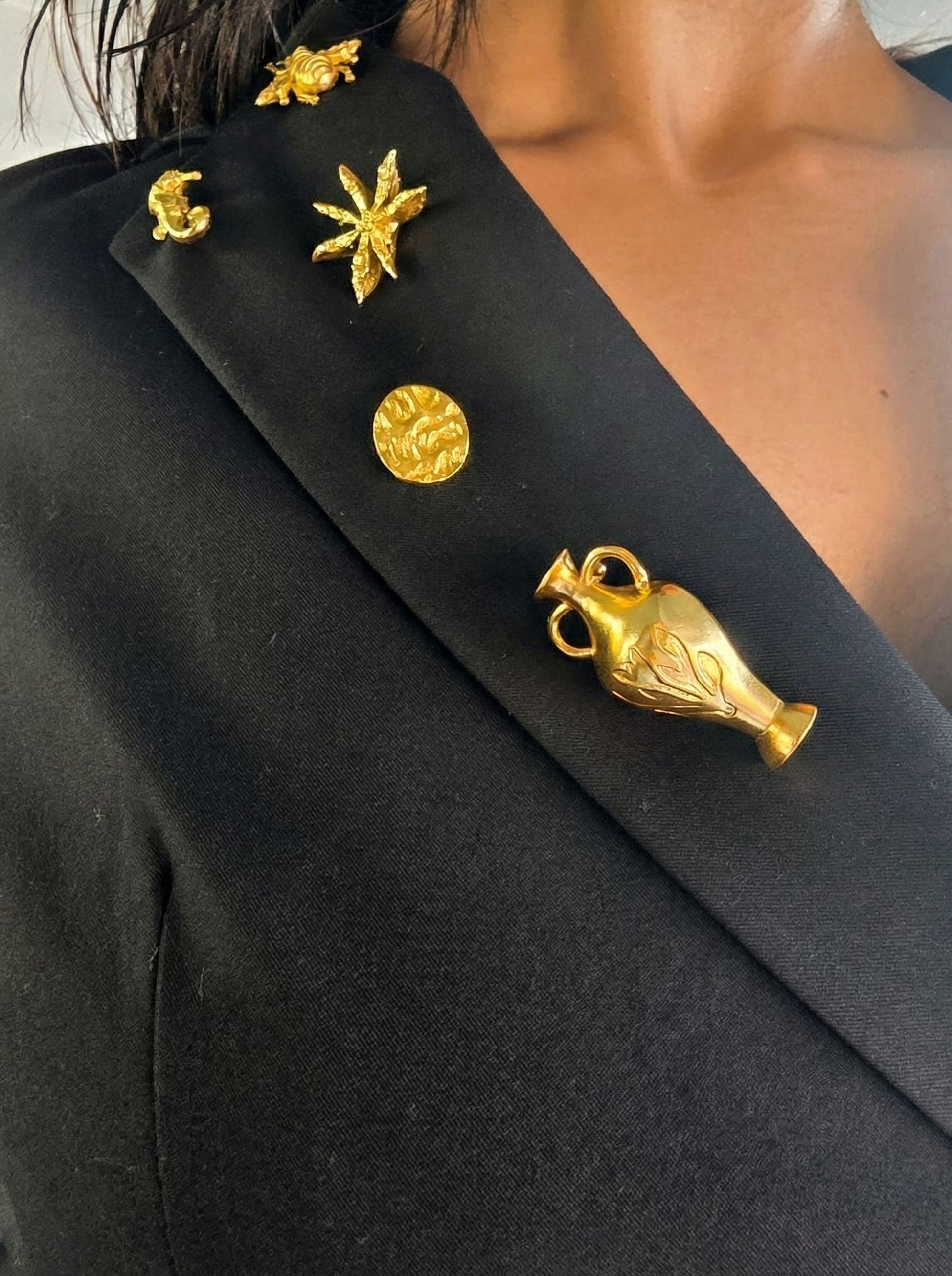 a close-up view of a person wearing a black blazer with several gold decorative pins or brooches pinned to the lapel.