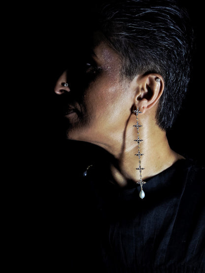 Near Earth Object | Close-up of an ear wearing a dangling earring with a dark background