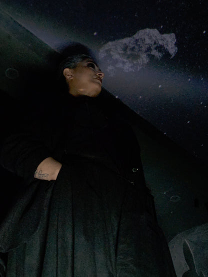 Near Earth Object | Person lying on a dark surface with a tattoo visible on their arm.