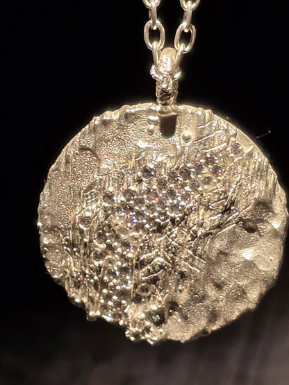 Near Earth Object | Close-up of a textured silver pendant on a chain against a dark background