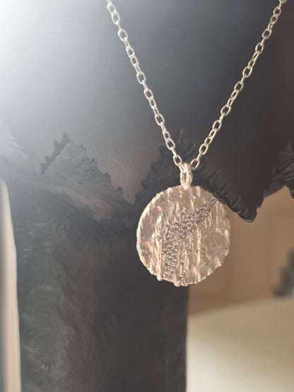 Near Earth Object | Silver necklace with a textured round pendant on a dark fabric background