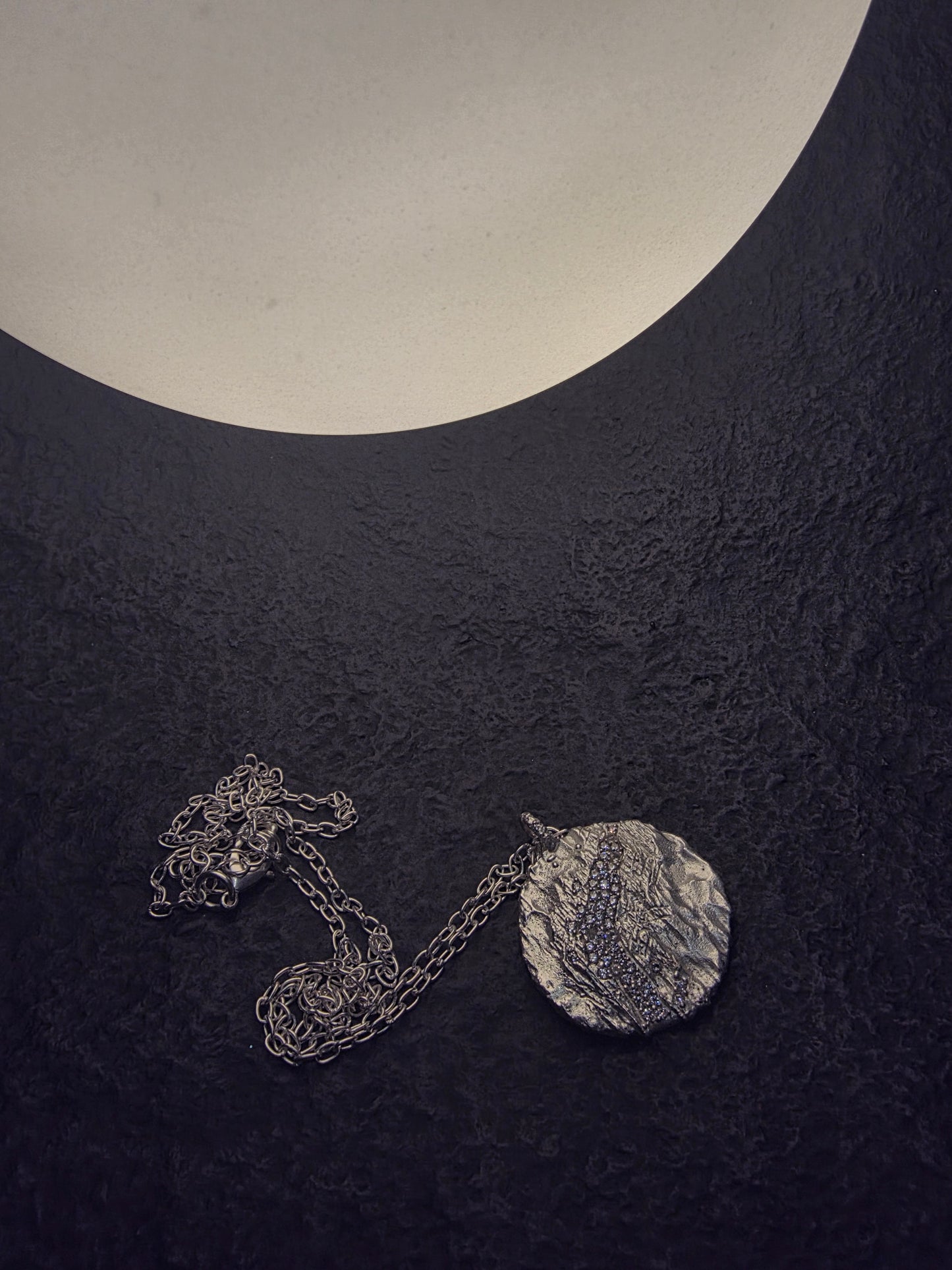 Near Earth Object | Silver necklace with a round pendant on a dark textured surface