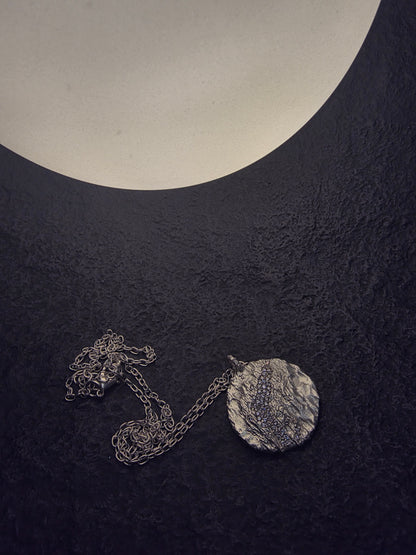 Near Earth Object | Silver necklace with a round pendant on a dark textured surface