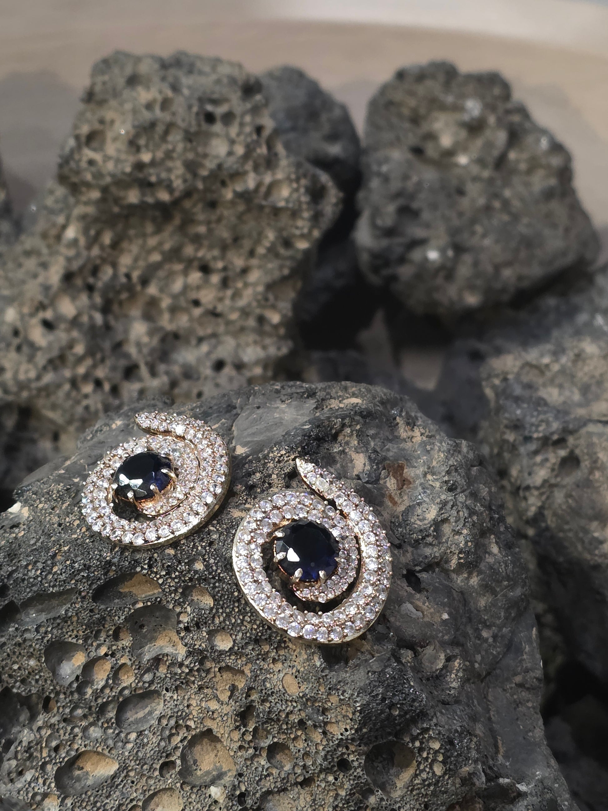 Near Earth Object | Pair of silver earrings with gemstones on a textured stone surface