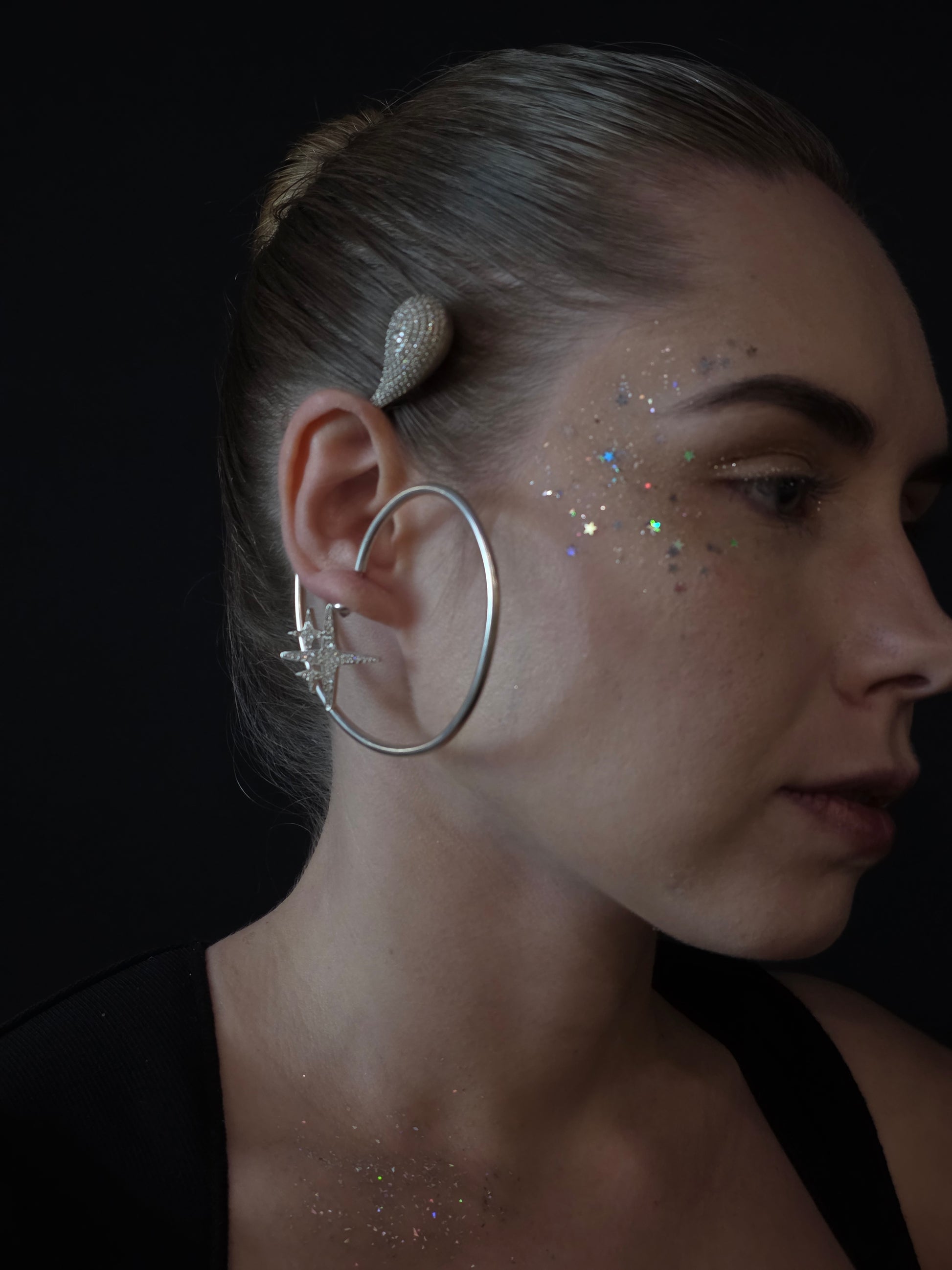 Near Earth Object | Close-up of a person wearing large hoop earrings with a dark background