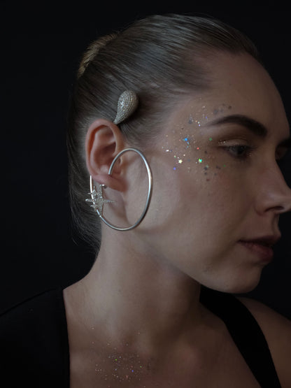 Near Earth Object | Close-up of a person wearing large hoop earrings with a dark background