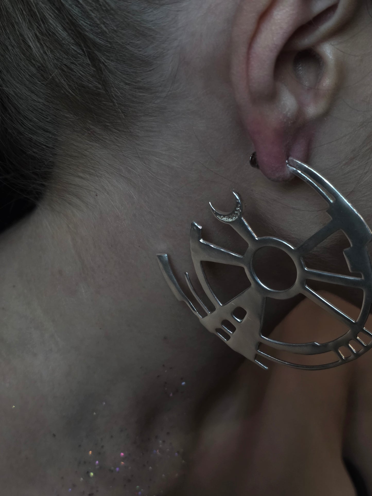 Near Earth Object | Close-up of a silver earring with a unique design worn by a person.