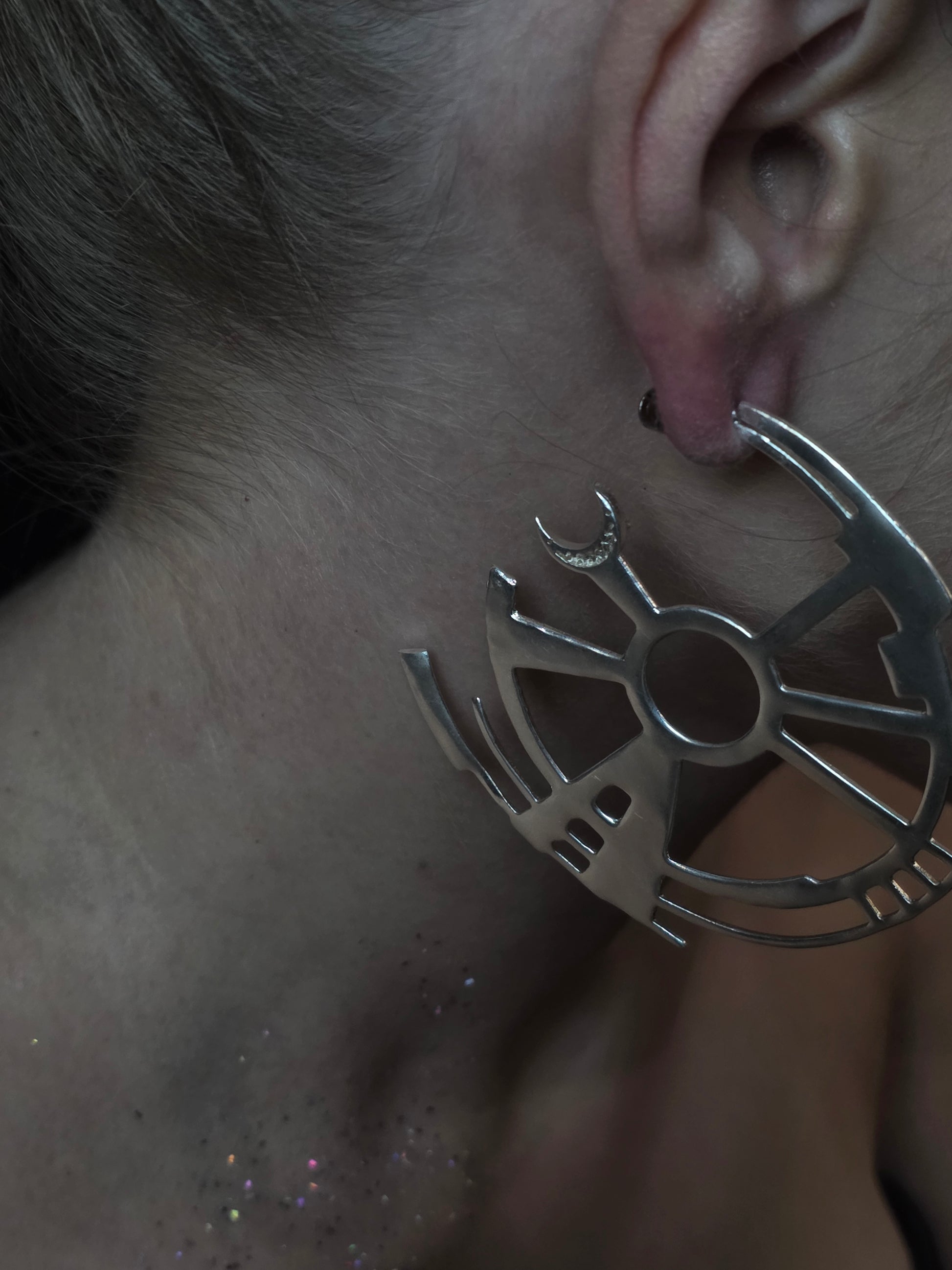 Near Earth Object | Close-up of a silver earring with a unique design worn by a person.