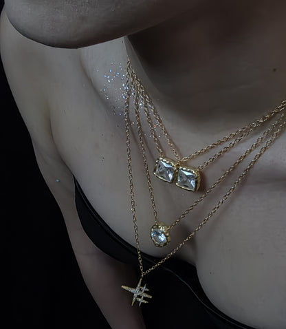 Near Earth Object | Close-up of a person wearing multiple gold necklaces with gemstone pendants on a dark background