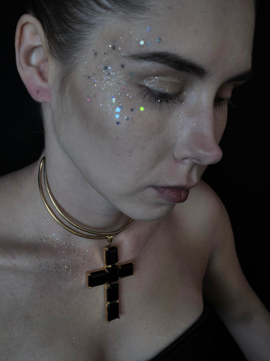 Near Earth Object Midnight Cross Choker featuring a bold black crystal cross pendant on a double-wrap gold snake chain, styled on model with glitter