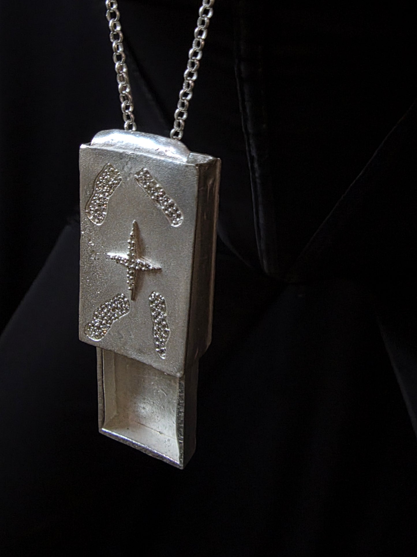 Near Earth Object | Silver pendant with star design on a chain against a dark background