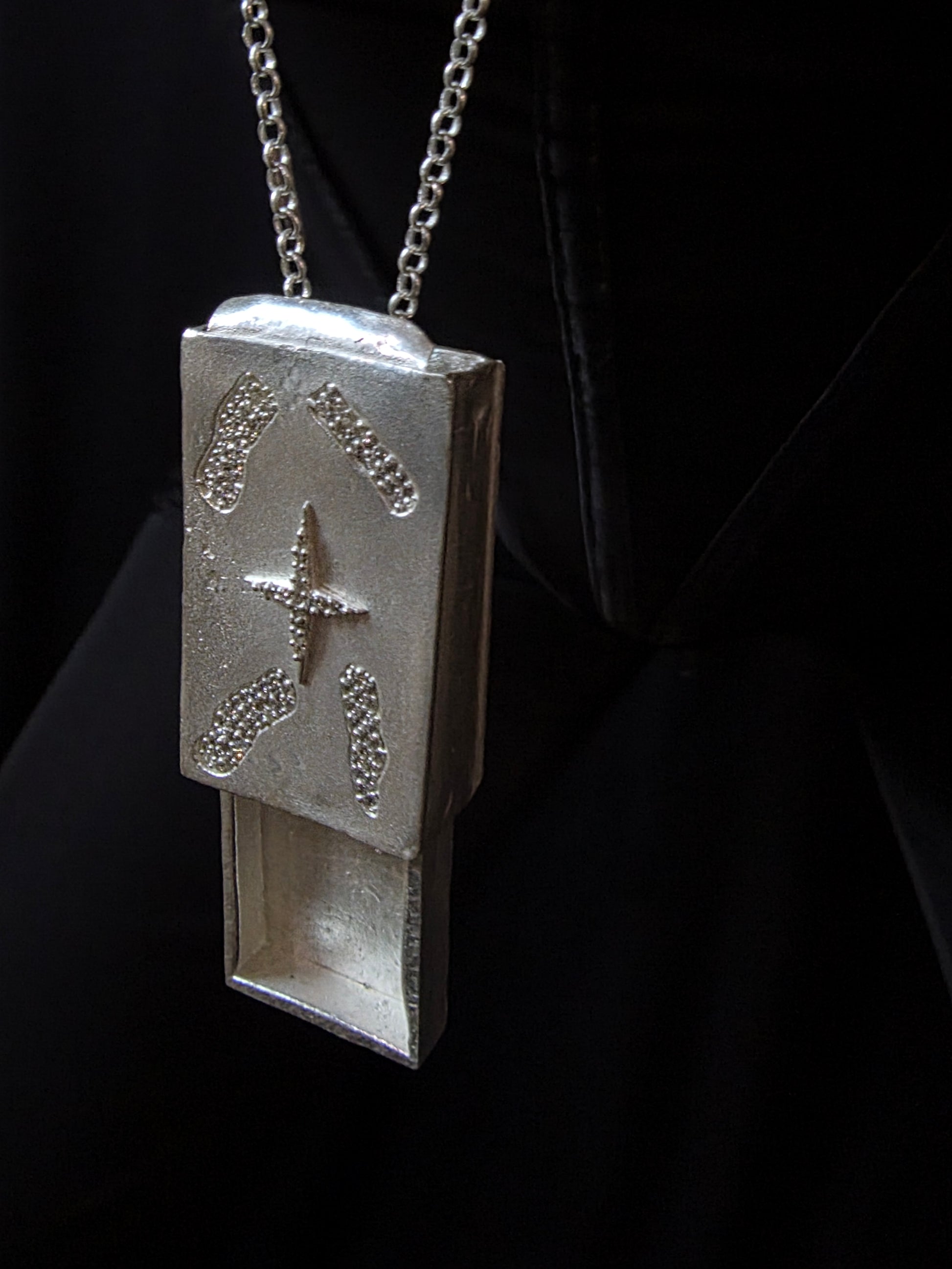 Near Earth Object | Silver pendant with star design on a chain against a dark background