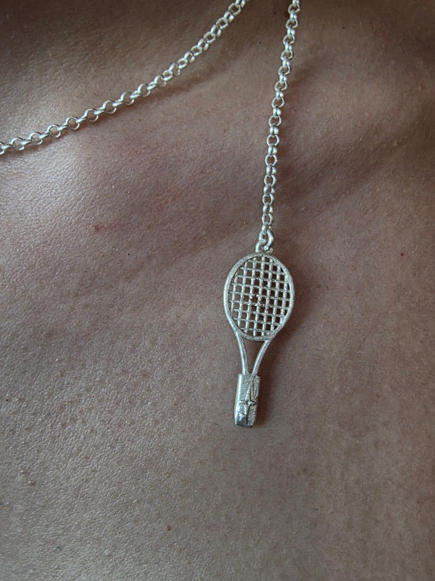 Near Earth Object | Silver tennis racket pendant on a chain against a beige background