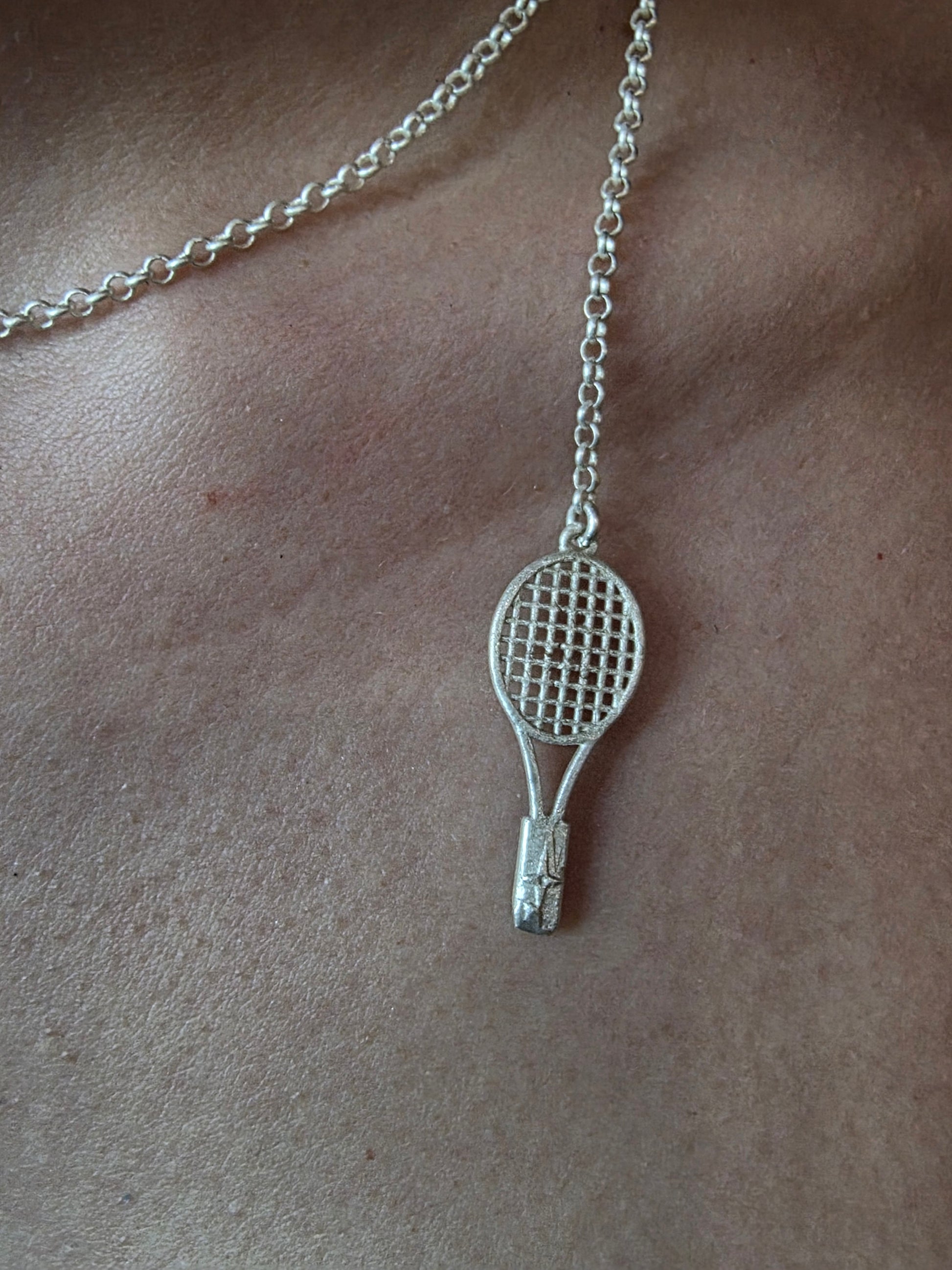 Near Earth Object | Silver tennis racket pendant on a chain against a beige background