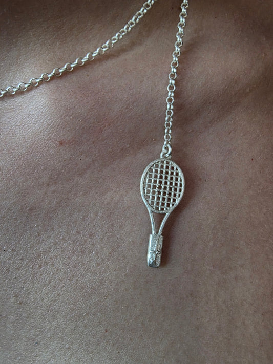 Near Earth Object | Silver tennis racket pendant on a chain against a beige background