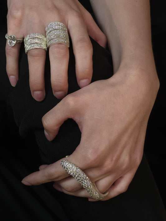 Near Earth Object | Close-up of hands wearing multiple diamond rings on a dark background