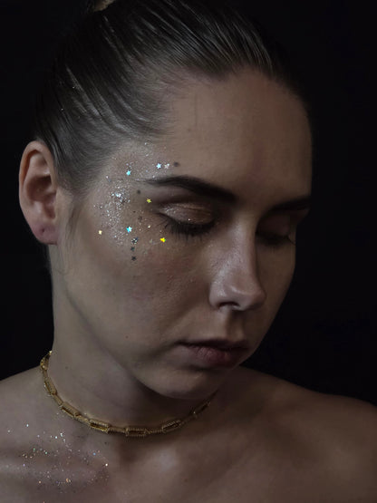 Near Earth Object | Close-up of a person with glitter on their face against a dark background
