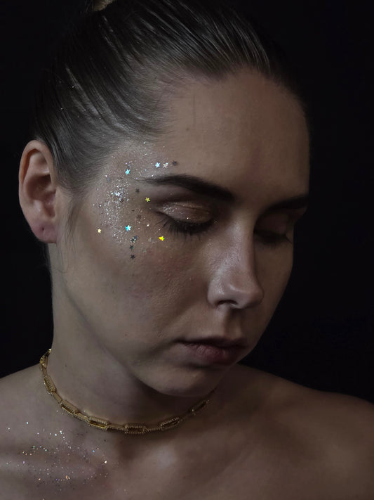 Near Earth Object | Close-up of a person with glitter on their face against a dark background