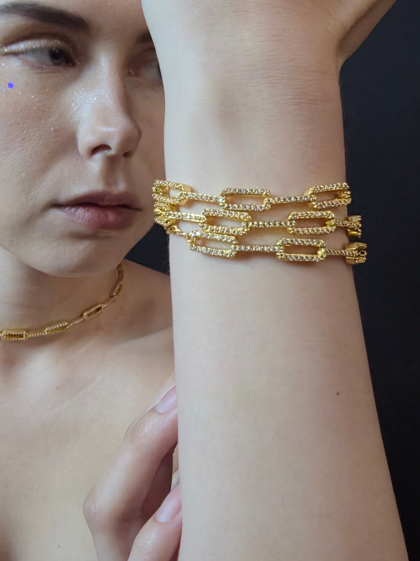 Near Earth Object | Close-up of a person wearing multiple gold chain bracelets on a dark background
