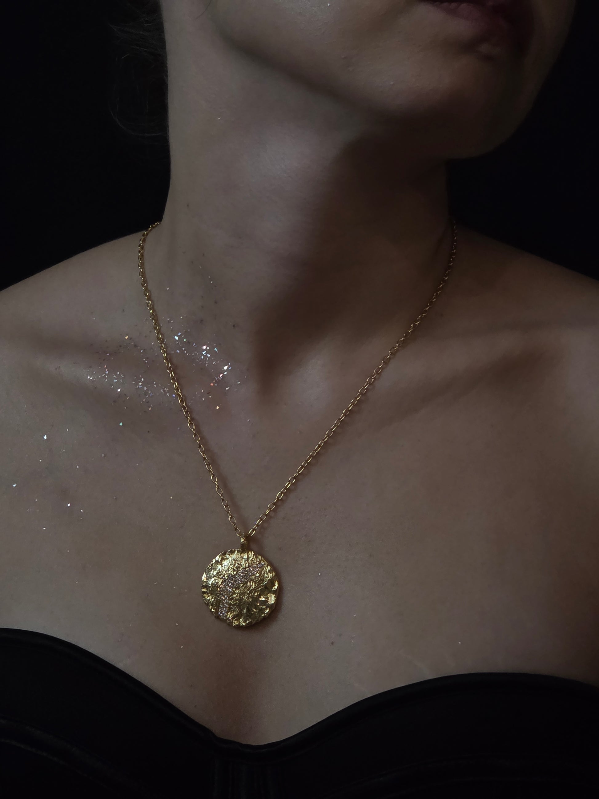Near Earth Object | Gold necklace with a decorative pendant on a person's neck against a dark background