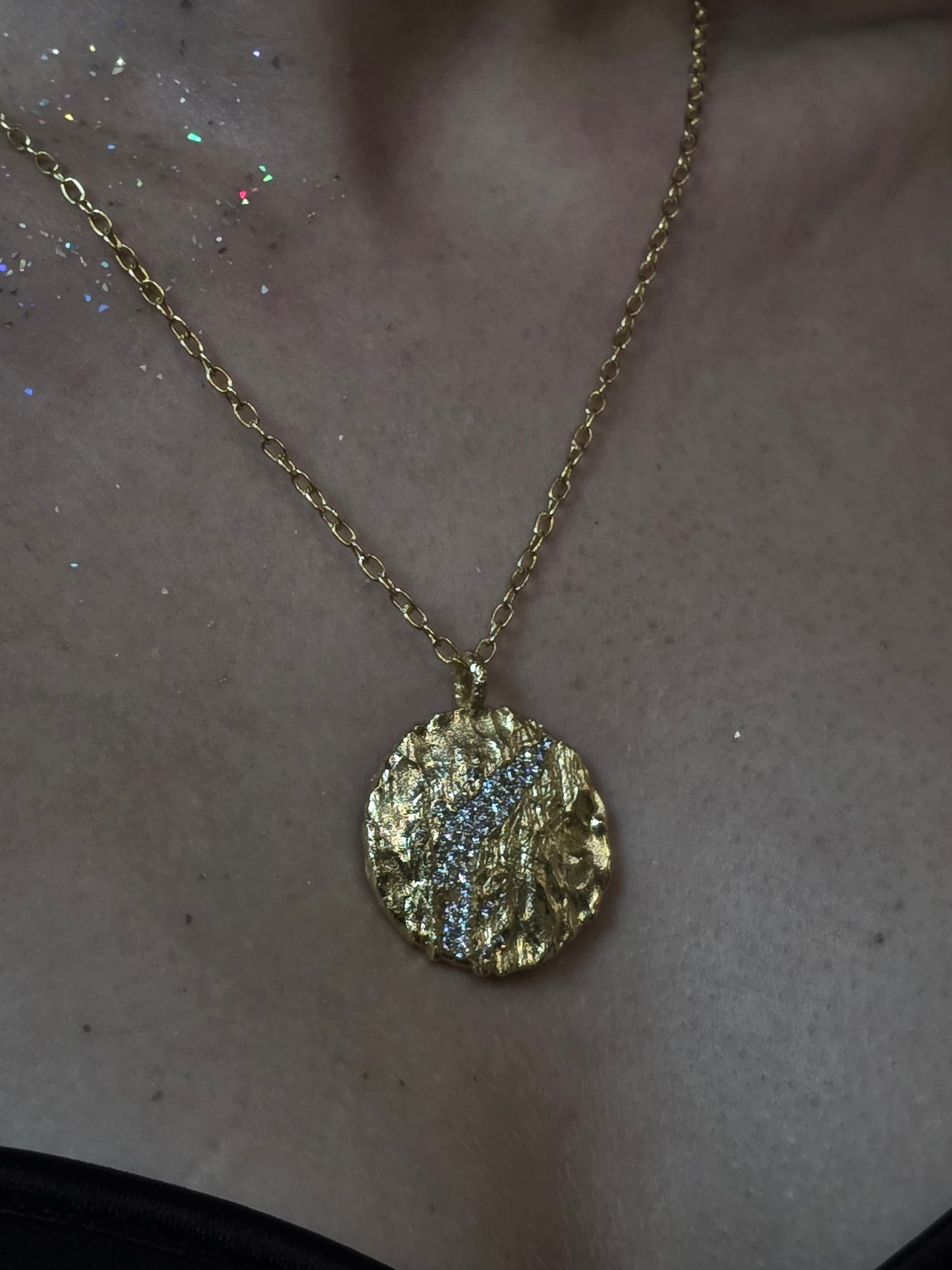 Near Earth Object | Gold necklace with a round, textured pendant on a neutral background