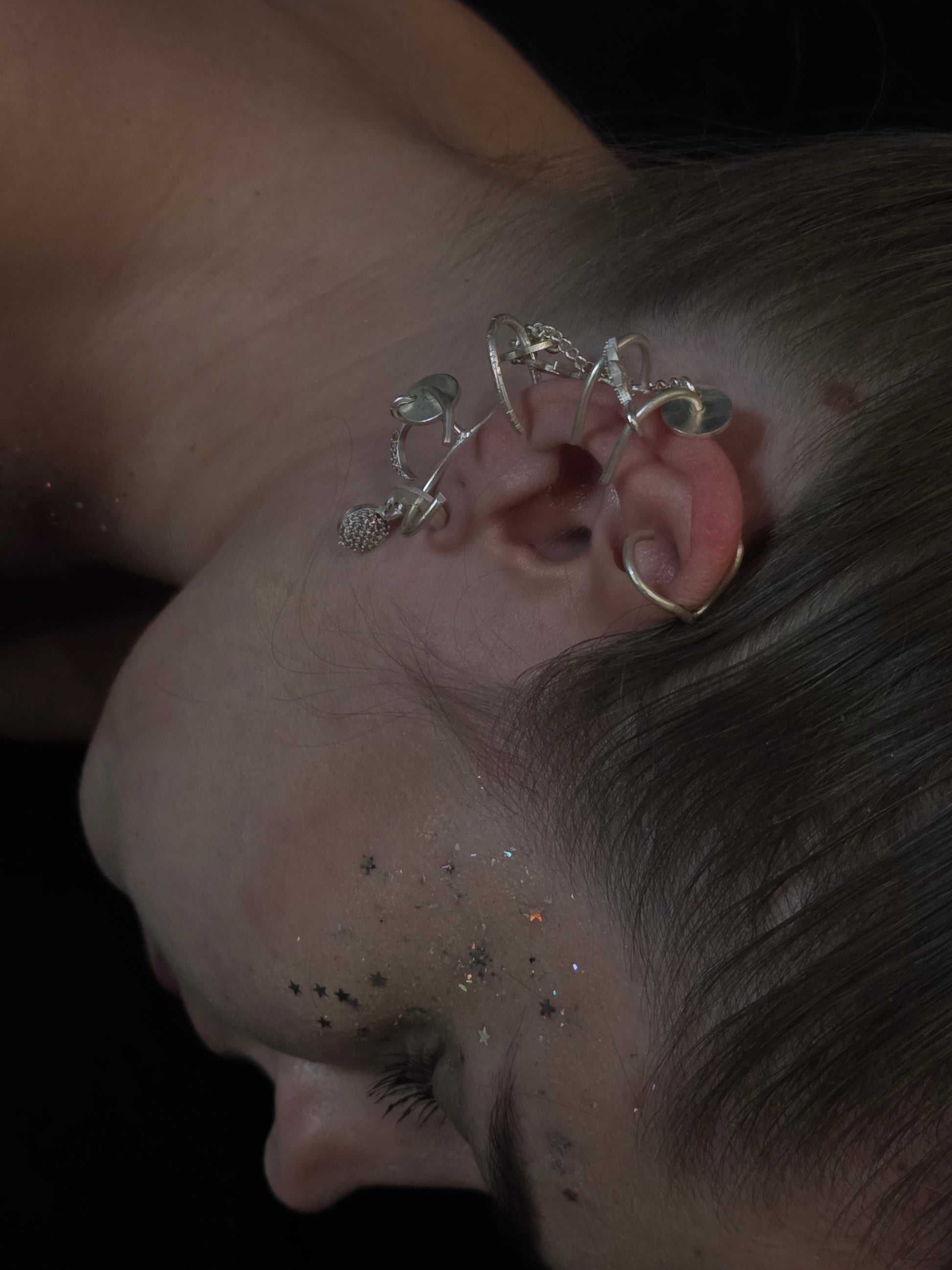 Near Earth Object | Close-up of an ear with a silver earring against a dark background