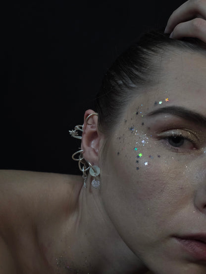 Near Earth Object | Close-up of a person's ear with earrings and glitter on a dark background