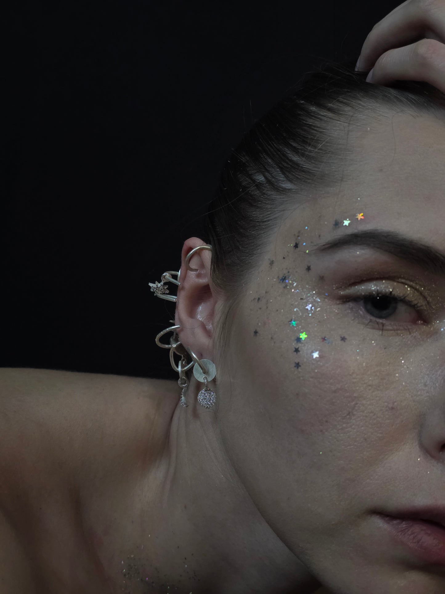 Near Earth Object | Close-up of a person's ear with earrings and glitter on a dark background