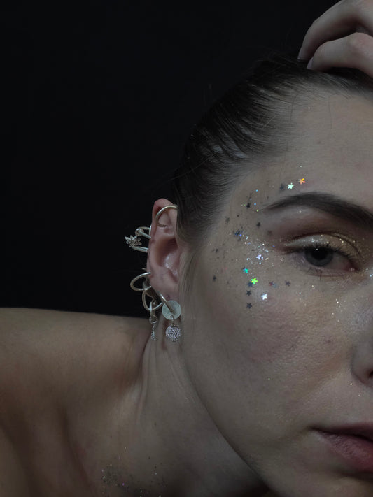 Near Earth Object | Close-up of a person's ear with earrings and glitter on a dark background