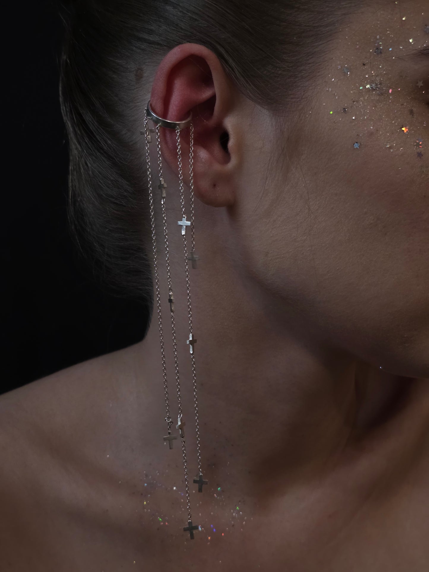 Near Earth Object Cross Cascade Cuff – statement silver ear cuff with cascading multi-chain drops and scattered mini cross pendants, styled on model with glitter makeup