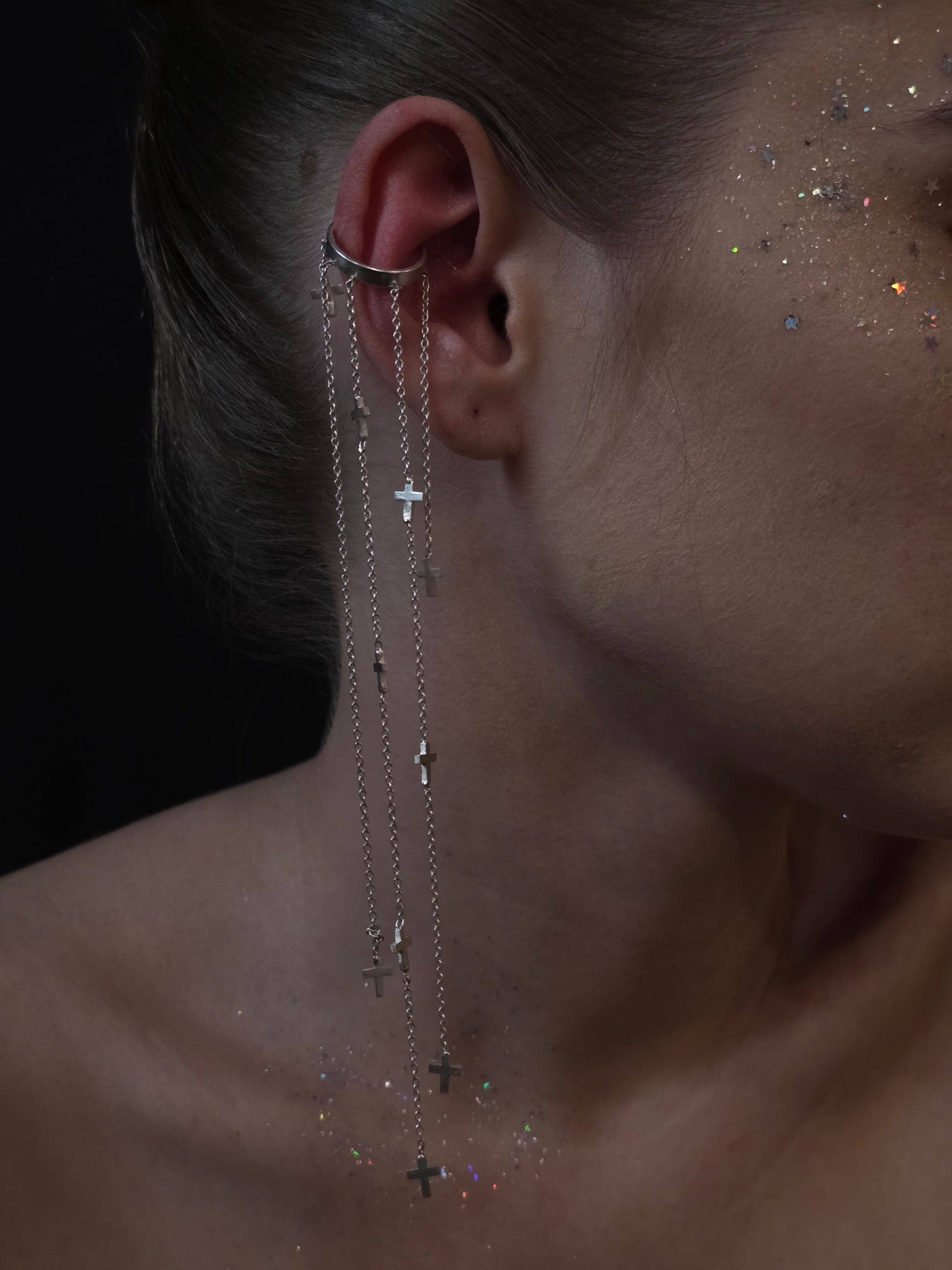 Near Earth Object Cross Cascade Cuff – statement silver ear cuff with cascading multi-chain drops and scattered mini cross pendants, styled on model with glitter makeup
