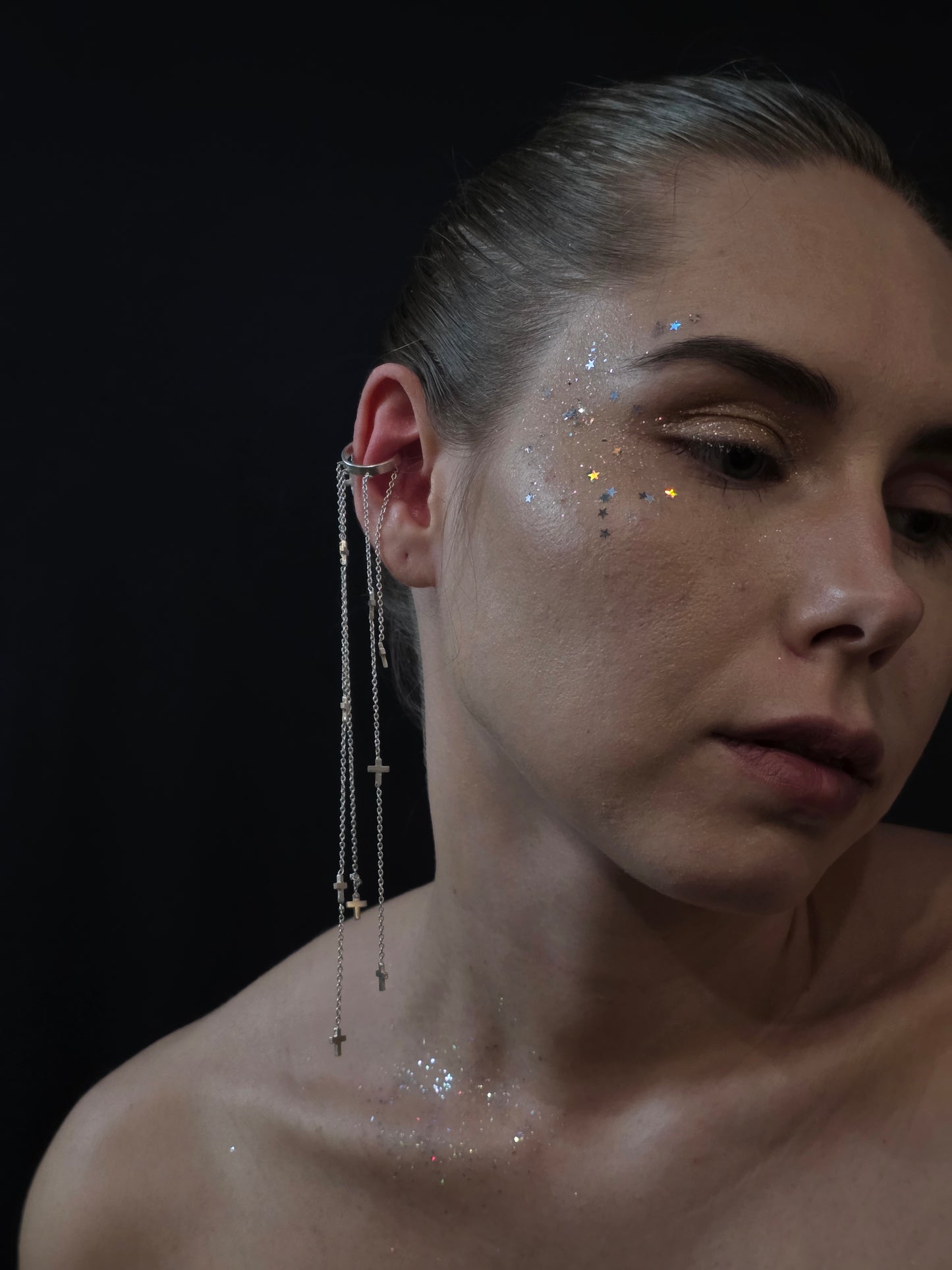 Near Earth Object Cross Cascade Cuff worn on model – dramatic silver multi-chain ear cuff with cross charms falling from ear to shoulder, paired with iridescent star glitter on cheek and décolletage
