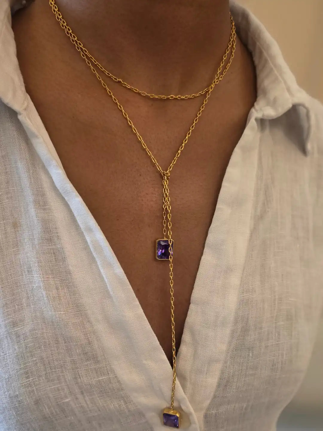 Gold necklace with a purple gemstone pendant worn by a person 