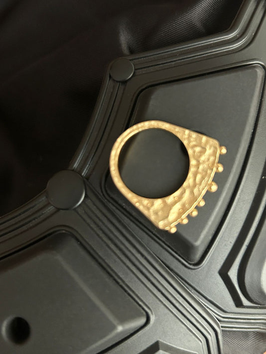 Gold crest ring with intricate sculptural detailing placed on black futuristic surface – premium jewellery by Near Earth Object.