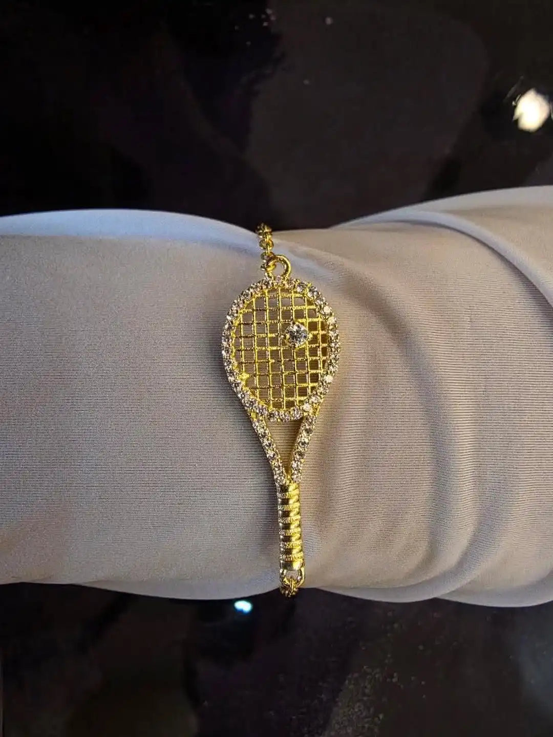 Gold bracelet shaped like a tennis racket on a wrist 
