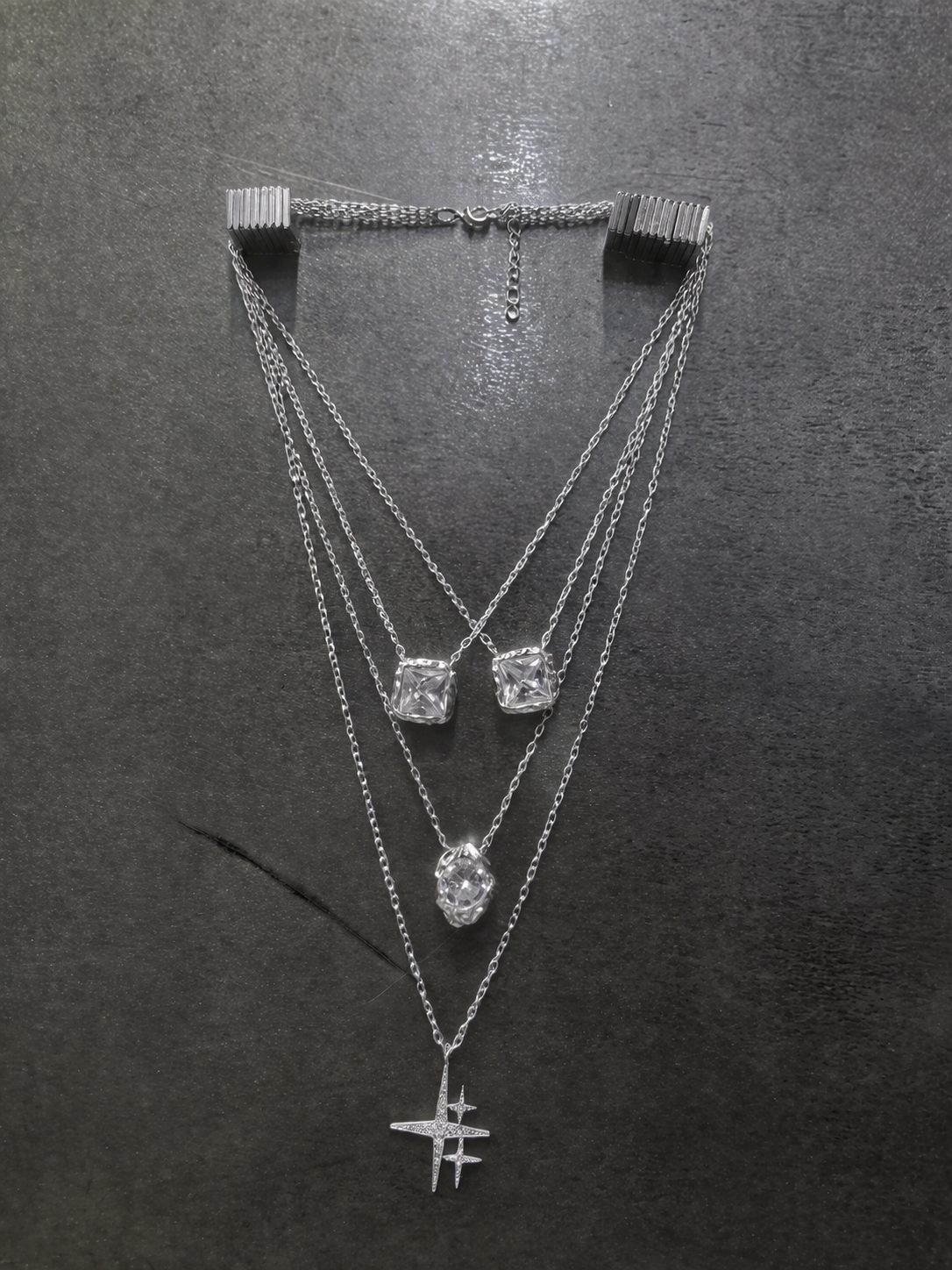 Near Earth Object | Three silver necklaces with various pendants on a dark surface