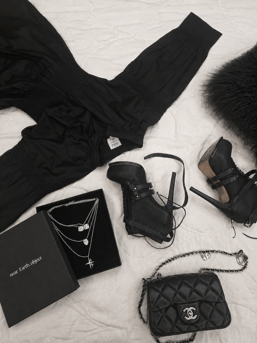 Near Earth Object | Black outfit with accessories including a handbag, boots, and jewelry on a light background
