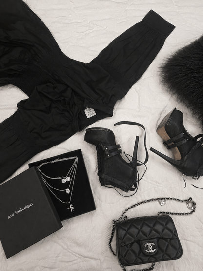 Near Earth Object | Black outfit with accessories including a handbag, boots, and jewelry on a light background
