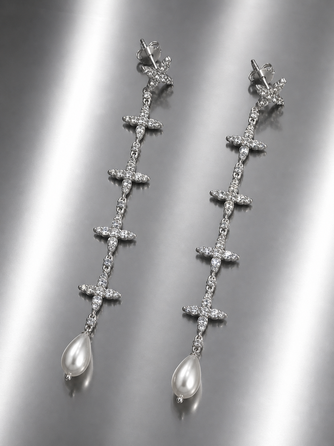 Near Earth Object | Silver cross-shaped earrings with pearl drops on a reflective surface