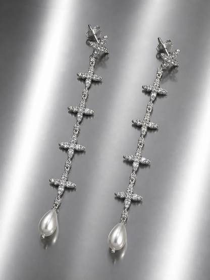 Near Earth Object | Silver cross-shaped earrings with pearl drops on a reflective surface