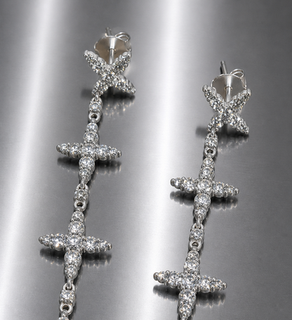 Near Earth Object | Silver cross-shaped earrings with clear stones on a reflective surface