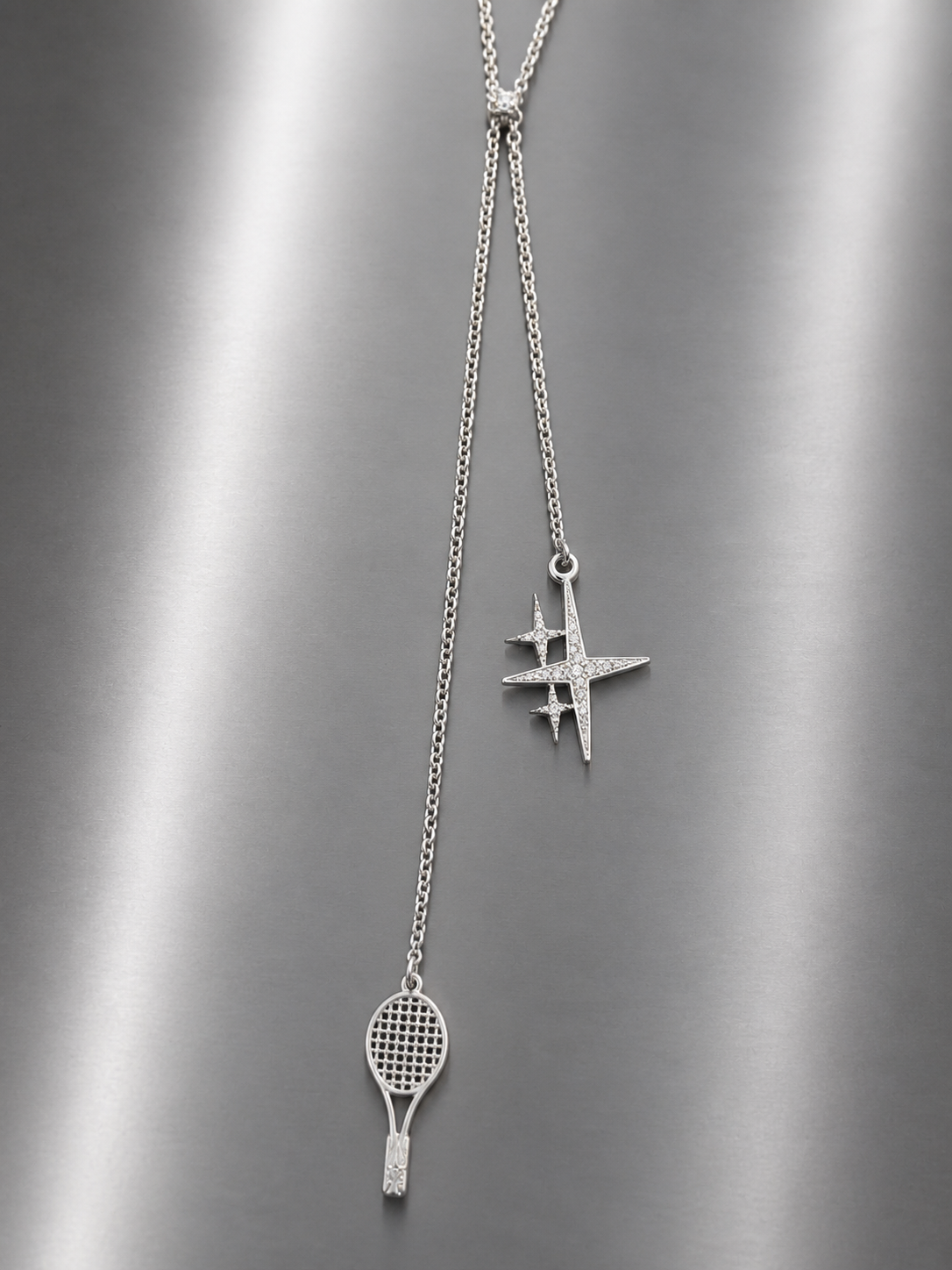 Near Earth Object | Silver necklace with tennis racket and hashtag pendant on a gray background