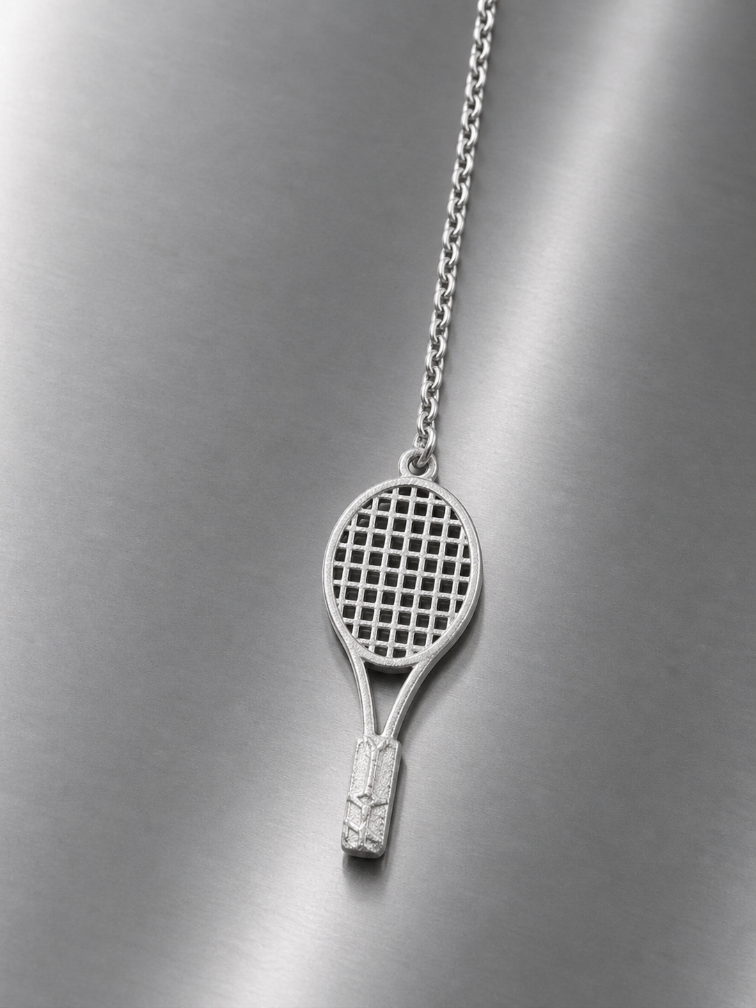 Near Earth Object | tennis racket pendant on a chain against a metallic background