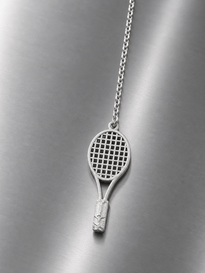 Near Earth Object | tennis racket pendant on a chain against a metallic background
