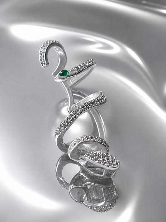 Near Earth Object | Silver snake-shaped brooch with a green gemstone on a reflective silver background
