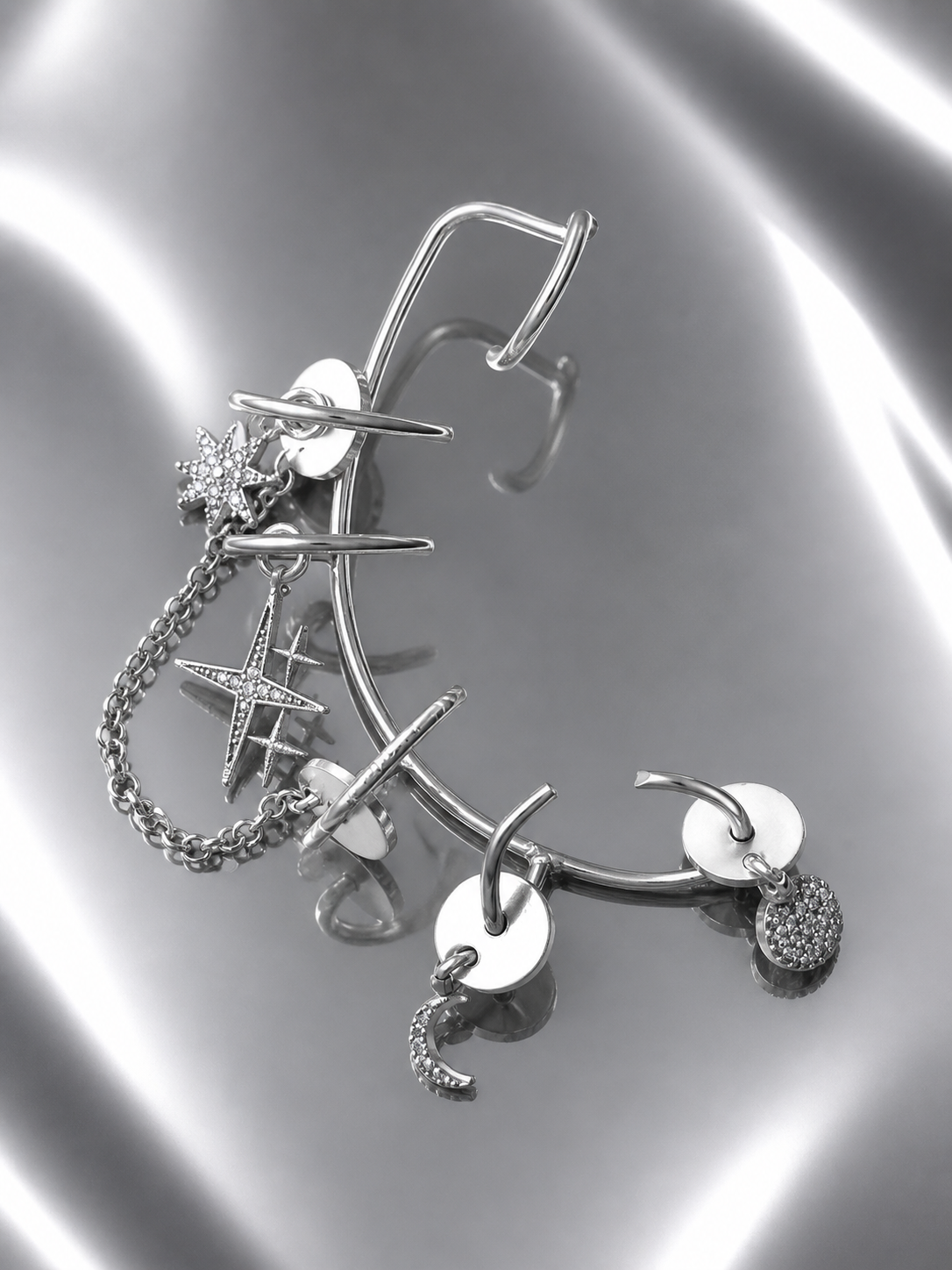 Near Earth Object | Silver earrings with various charms on a reflective surface