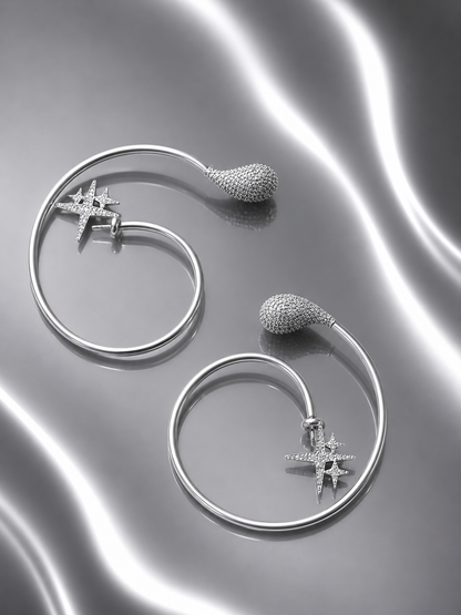 Near Earth Object | Silver hoop earrings with star and sphere designs on a reflective surface